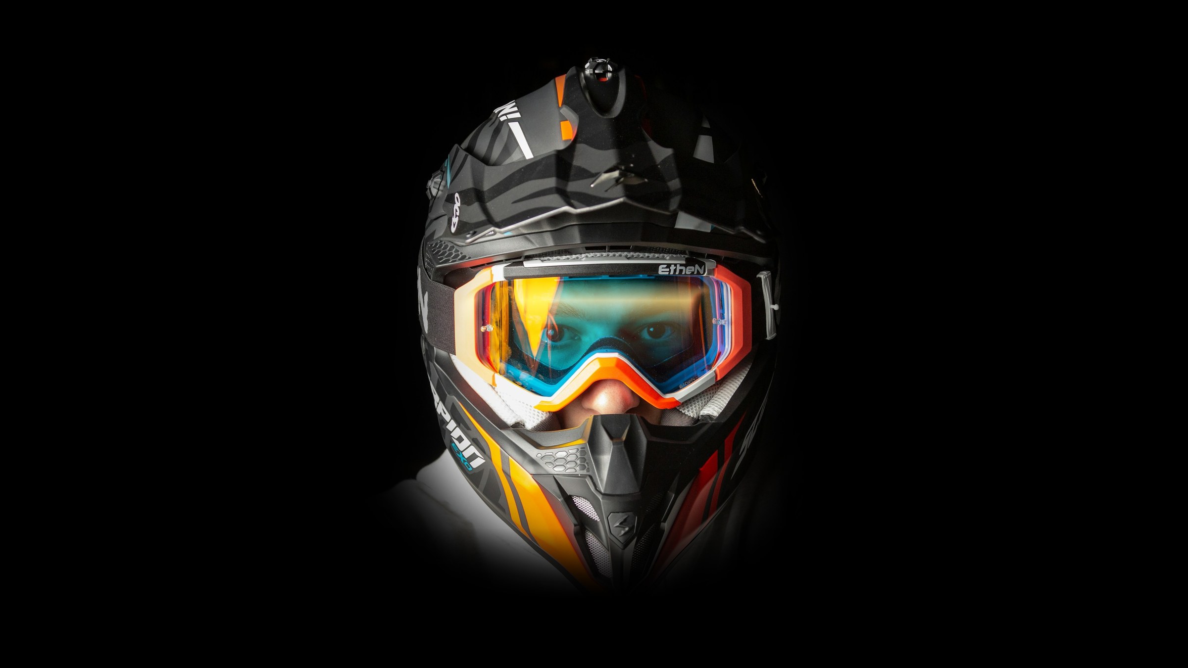 Close-up of a motocross helmet and goggles on a black background